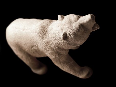 Eine kleine, hellfarbene Bärenfigur, die aufrecht steht und den Kopf hebt.