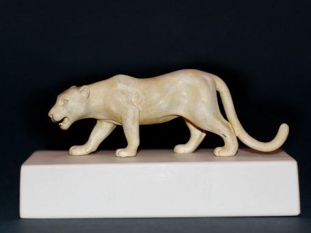 Schnitzerei einer Katze in seitlicher Ansicht, auf einem weißen Sockel.