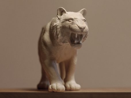 Eine graue, detaillierte Statue eines knurrenden Tigers vor neutralem Hintergrund.