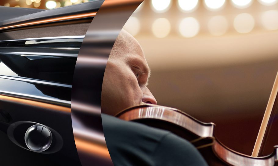 Mann spielt Geige, im Hintergrund unscharf ein Klavier und Bühnenlichter.