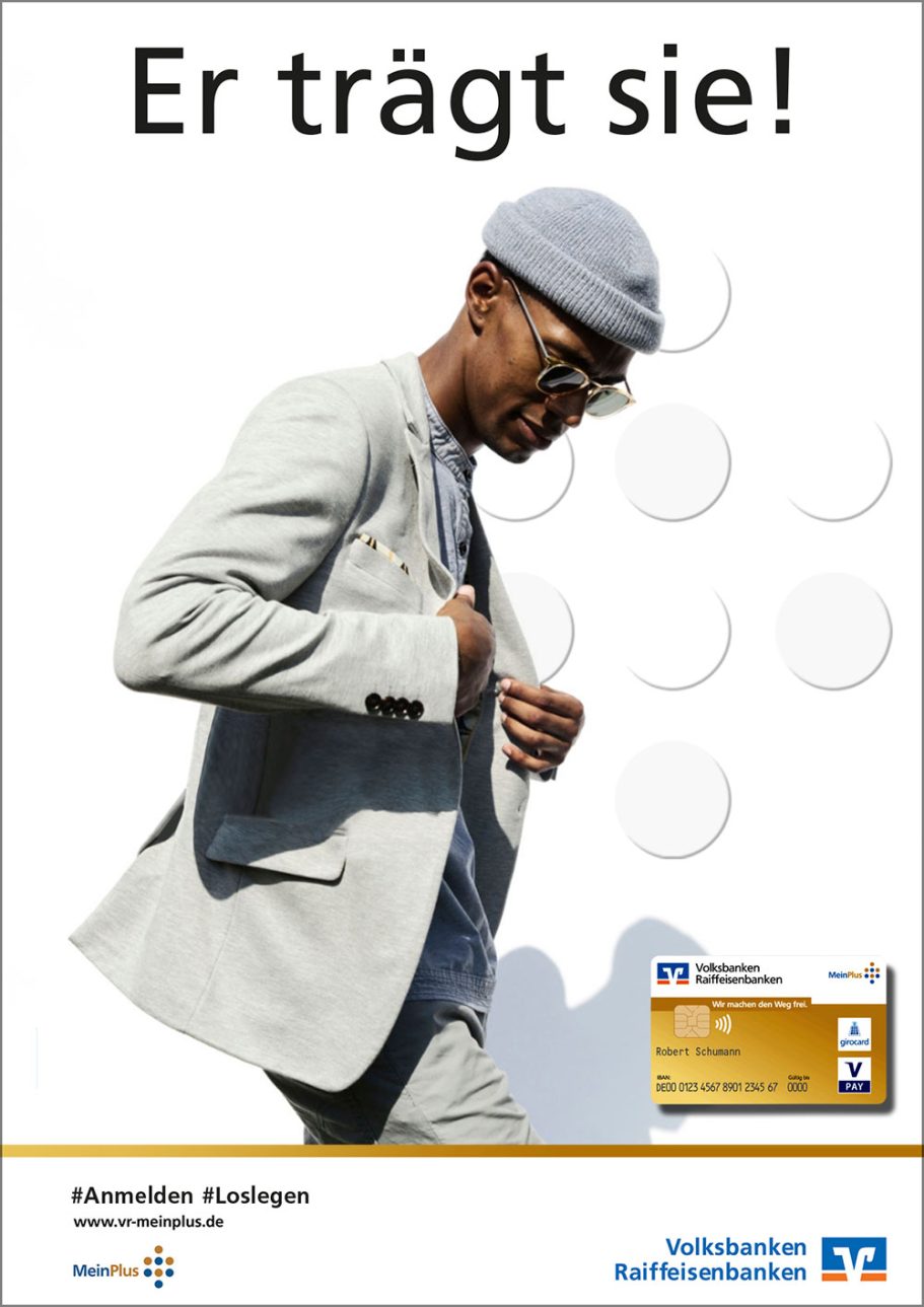 Großbildfläche - MeinPlus Mann in heller Anzugjacke und Hut, der einen kleinen gelben Gegenstand hält.