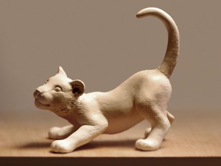 Schnauziger, spielender Kater aus hellem Keramikmaterial.