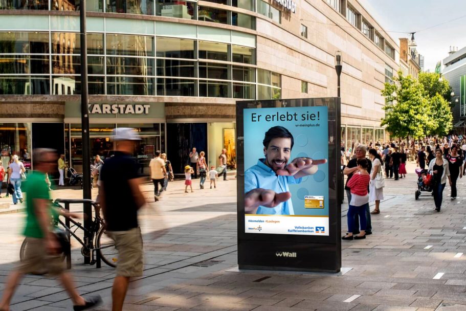 Citylight Menschen auf einer belebten Straße, Werbung auf einem digitalen Display im Vordergrund.